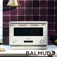 The Range 20L微波烤箱，米白色機身，配有銀色金屬把手。正面有黑色玻璃門、顯示螢幕及操作旋鈕和按鈕。背景是深紫色方形磁磚牆。