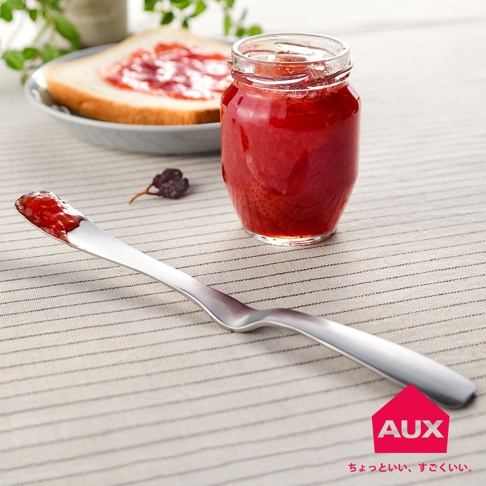 金屬抹刀沾有紅色果醬，刀身呈銀色，旁邊有一個裝有紅色果醬的玻璃罐，背景是塗抹了果醬的吐司片。