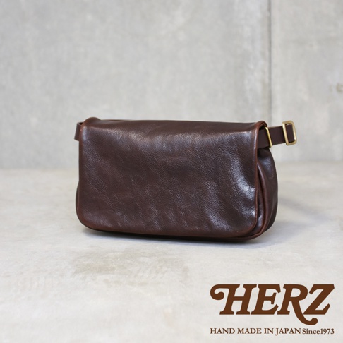 深棕色皮革製成的斜背包，側面可見金屬扣環，包身線條圓潤，展現職人手作質感。