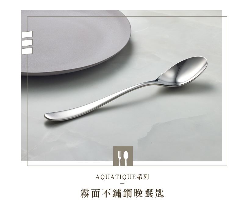 霧面不鏽鋼晚餐匙，帶有優雅的曲線，放置於灰色盤子旁。