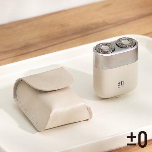 一個米白色便攜式刮鬍刀，配有銀色頂蓋和兩個圓形刀頭，旁邊是一個米白色的皮質收納袋，產品上印有 ±0 SELECT 字樣。