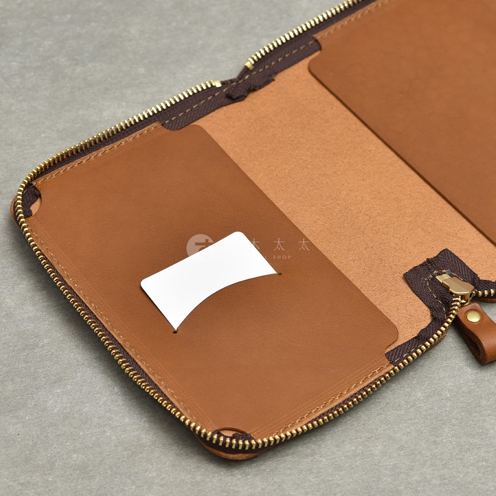 一個打開的棕色皮革記事本收納包，內有卡片插槽和拉鍊。