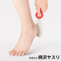 一只手持著譽HOMARE完美弧度磨腳器，該磨腳器為銀色金屬材質，帶有紅色圓形握把，正靠近一隻女性的右腳後跟。