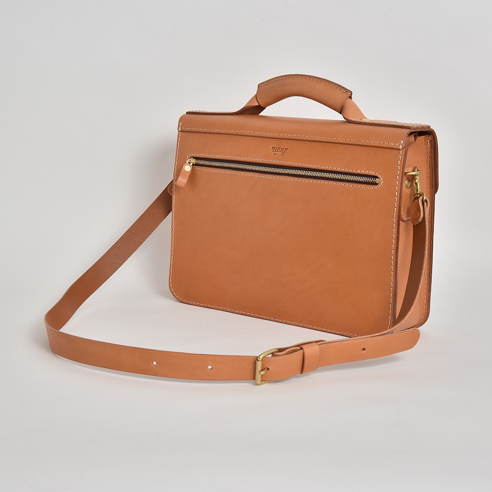 原色皮革學院風格兩用商務公事包，配有頂部提把、可拆卸肩帶及黃銅色拉鍊，展現精緻手工與耐用材質。