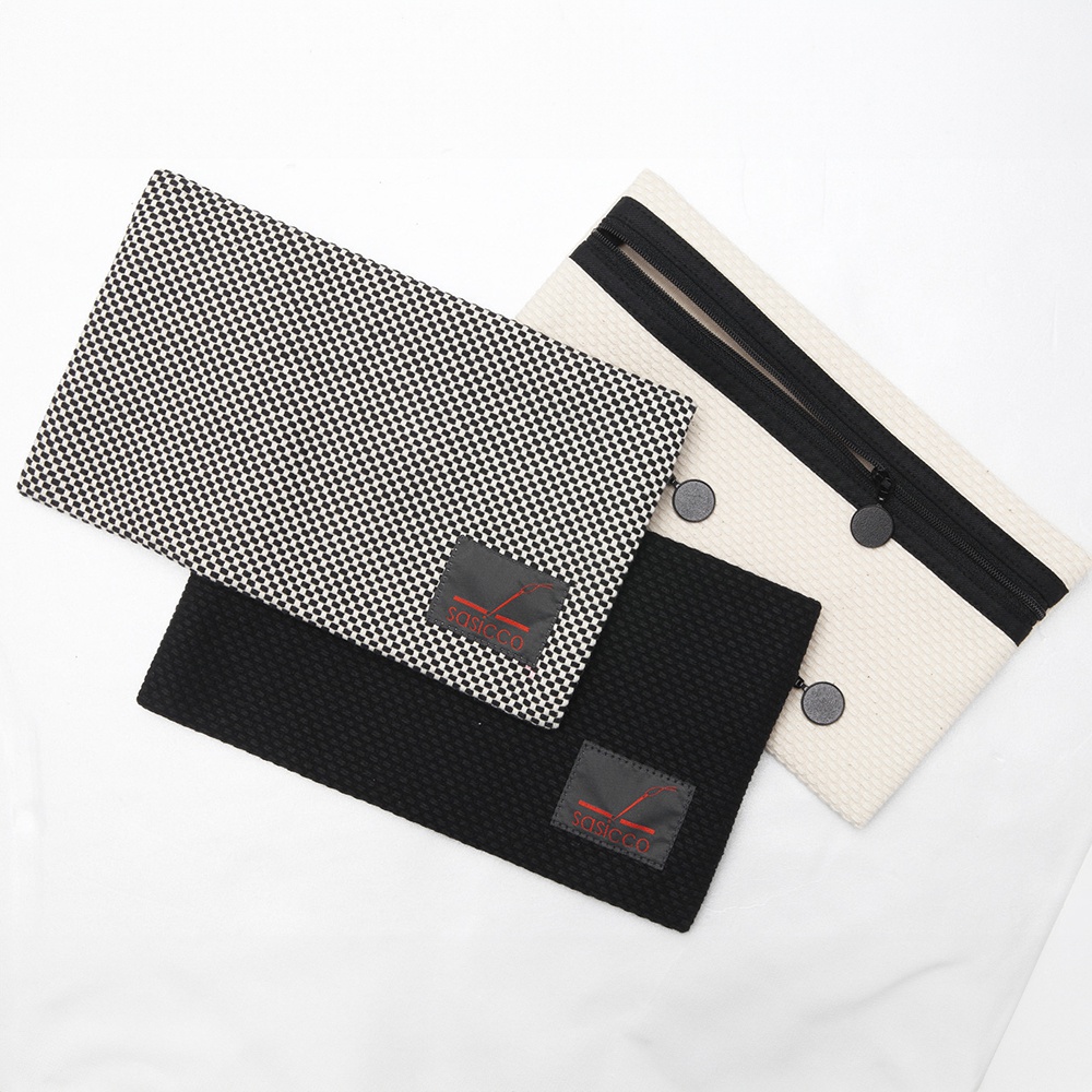 三河木綿刺子織文件收納包，展示黑白格紋、純黑與米白色三款。皆有品牌標籤，米白色款配有黑色拉鍊及兩顆黑色按扣。