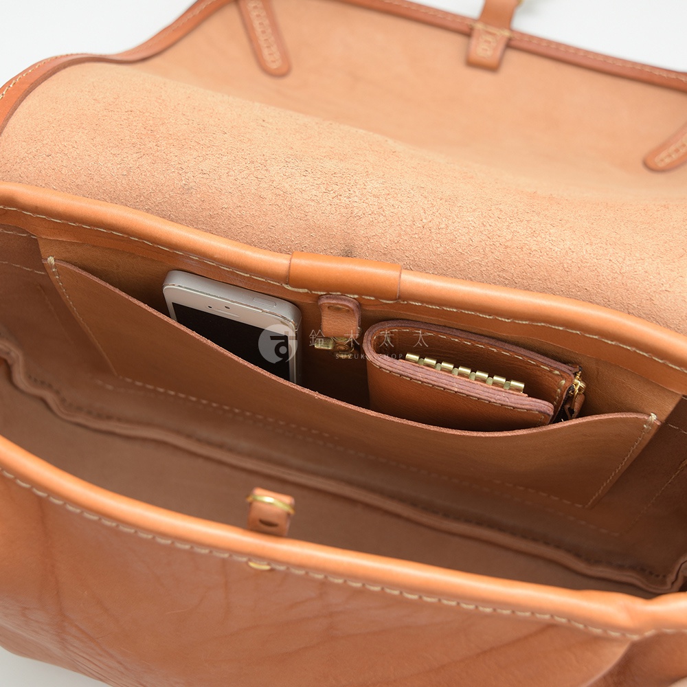 淺棕色皮革郵差包內部，可見手機、鑰匙包，以及多個隔層。