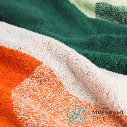 毛巾特寫，可見橘色、白色、深綠色和淺綠色條紋，右下角有 Murakami Pile 的品牌標誌