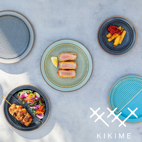 展示美濃燒瀝油餐盤，包含藍綠色、深灰色及藍色盤子，盤中皆附有金色或銀色瀝油金屬網。其中盤子上擺放了炸物、沙拉和烤肉串，盤邊有檸檬片。