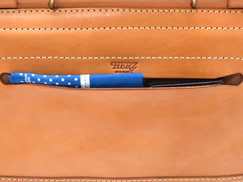 職人手作皮革屋瓦風兩用側背包 (CW-147) M，淺棕色皮革，正面有一個藍色圓點圖案的布料與一支黑色筆，皮革表面有細緻縫線，並壓印有「HERZ」品牌標誌。