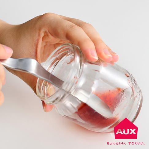 手持金屬果醬抹刀，正在從裝有紅色果醬的透明玻璃罐中取出果醬。