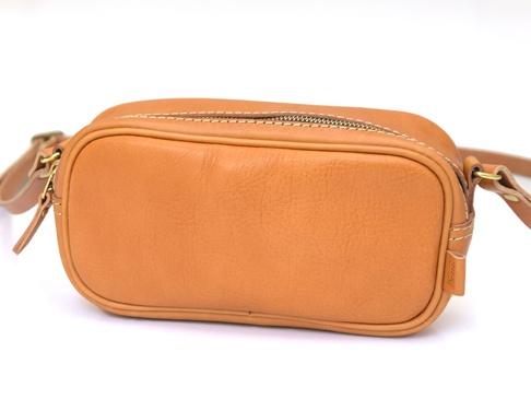 職人手作的棕褐色皮革小方包，設有拉鍊開合和可調節的皮革肩帶，包身線條簡潔，皮革表面帶有自然紋理。