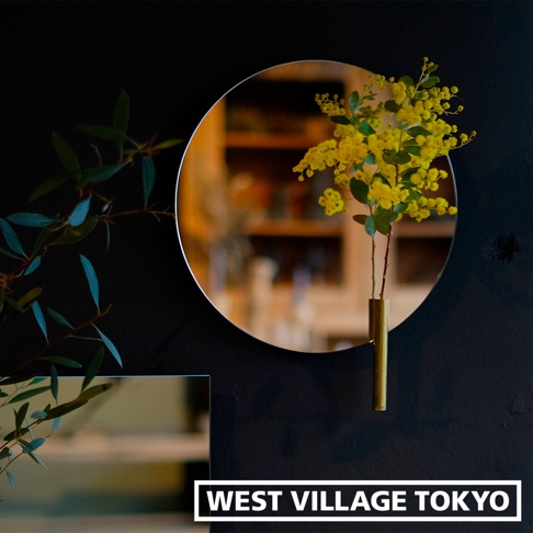 圓形鏡面壁掛花器，黃色小花束置於金色圓柱形花瓶中，與左側的綠色枝葉相互映襯。