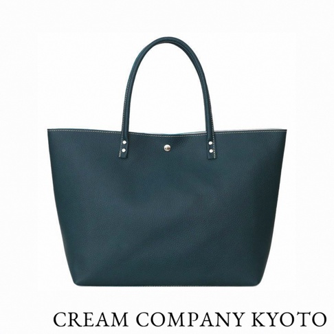 這是一款由京都品牌 CREAM COMPANY KYOTO 推出的簡約深藍色托特包，採用輕量耐用的 glove 牛皮革製作，外觀呈現經典的梯形輪廓，包身中央配有一顆金屬按扣，並以鉚釘固定提把，設計質感細膩且適用於休閒或商務場合。