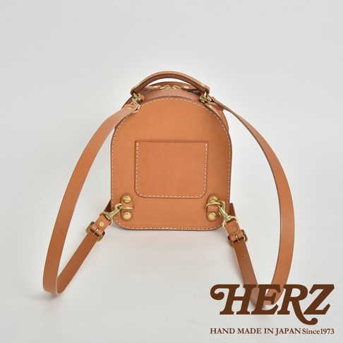 職人手作皮革迷你後背包，採用天然牛皮，呈現溫潤的焦糖棕色。圓潤的包身設計，正面有一個方形皮貼，搭配金屬扣環與可調式皮革背帶。