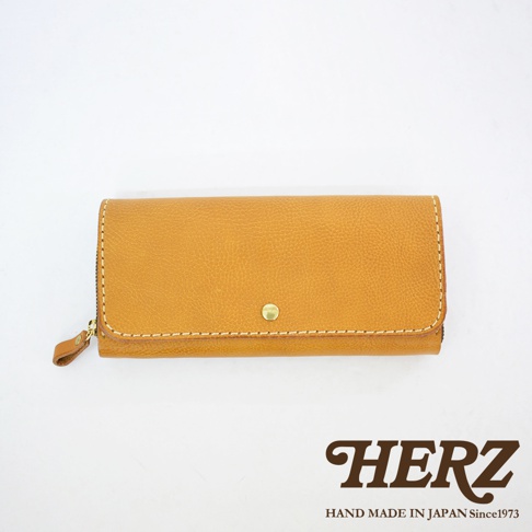 職人手作皮革長夾，焦糖棕色，寬口設計，側邊有拉鍊，正面有一個金色金屬釦，車縫線為米白色。