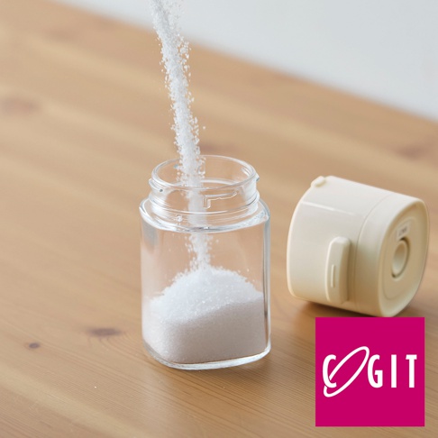 透明玻璃製的定量灑鹽罐，裝有白色細鹽，旁邊是米白色按壓式瓶蓋，整體放置在木質桌面。