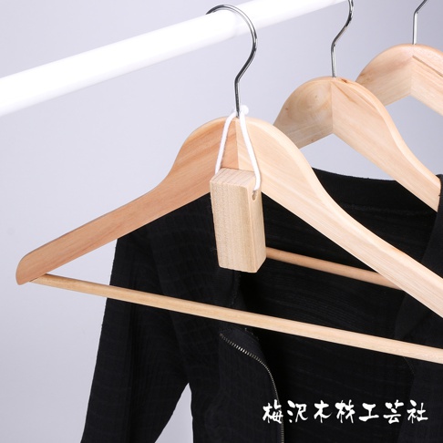 木製衣架上懸掛著一個小巧的淺棕色長方形樟木塊，用白色細繩綁住。背景為淺灰色。