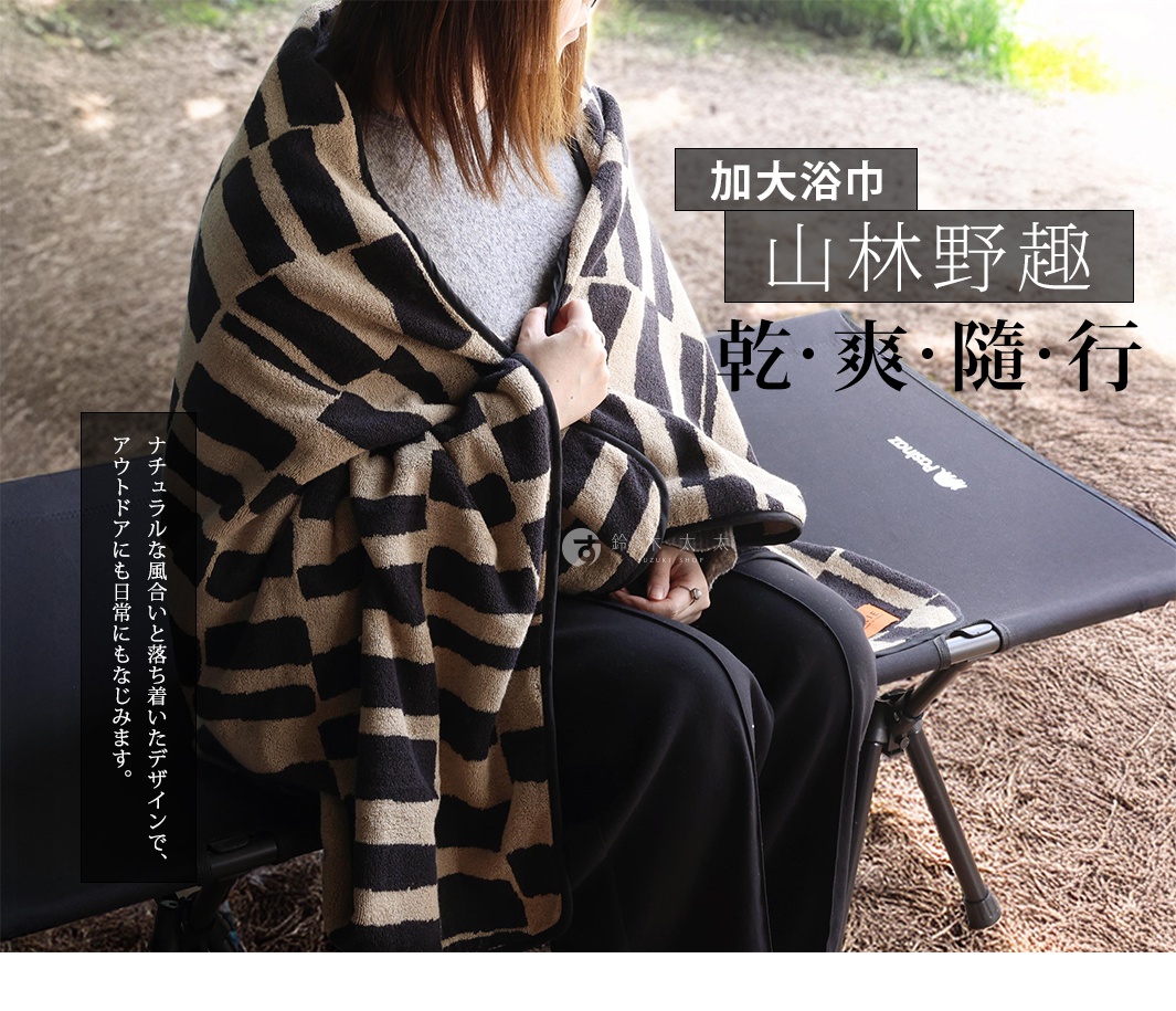 一位女性披著一條黑米格紋的毛巾，坐在一個戶外折疊椅上，毛巾上印有日文文字。