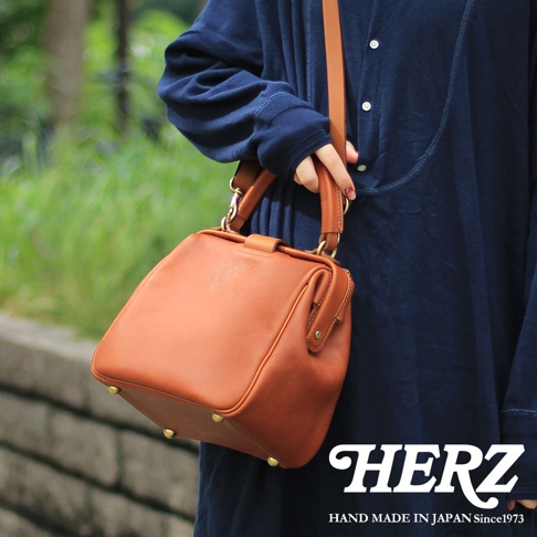 棕色皮革手提包，方形口金設計，配有手提把和斜背帶，包身有金屬腳釘裝飾。