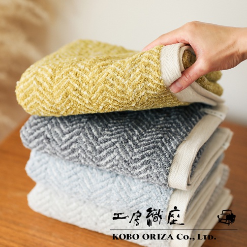 疊放的 SUFFICE 棉麻混紡毛巾，有黃色、灰色和淺藍色。毛巾表面有斜紋編織圖案，觸感蓬鬆，邊緣有米白色滾邊。