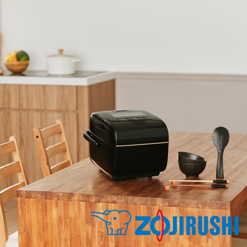 炎舞壓力IH電子鍋(NW-LAF10)為黑色，設有銀色飾條，搭配黑色飯勺、兩個黑色小飯碗及一雙木質筷子，擺放在木質餐桌上。