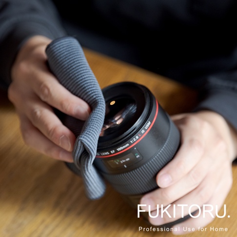 一雙手正用灰色超細纖維清潔布擦拭黑色相機鏡頭。