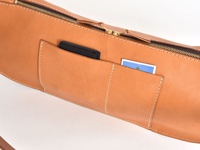 棕色皮革斜背包，特寫鏡頭展示外部口袋，其中一個口袋內有黑色手機，另一個口袋內有藍色卡片。包包採用縫線裝飾，配有金色拉鍊。