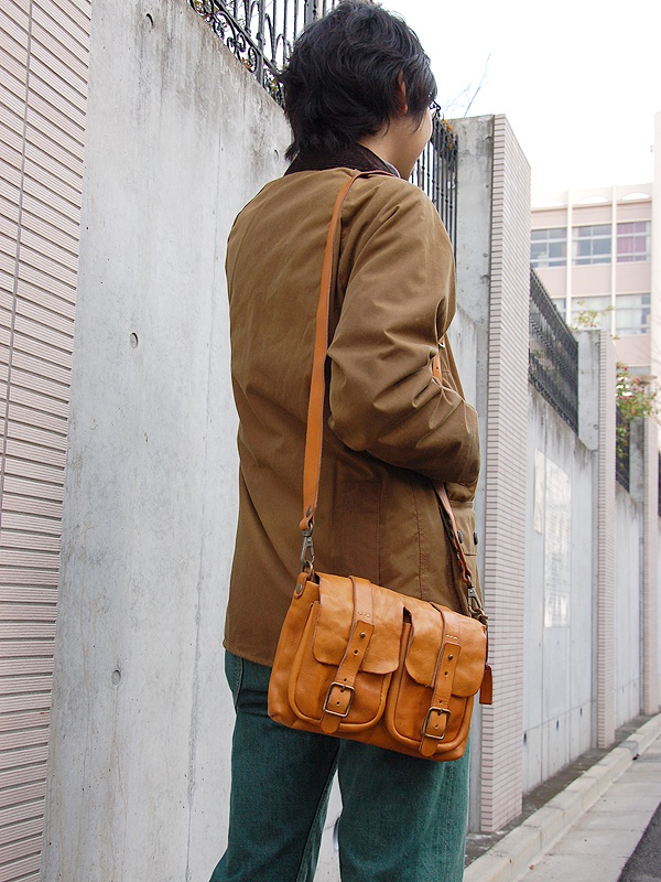 咖啡色皮革雙口袋肩背包，帶有兩個翻蓋和金屬扣環，側邊有可調節的皮革肩帶。