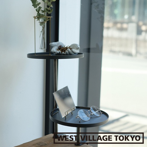 一組兩個黑色鐵製可夾式小物高低桌，上層擺放著玻璃瓶植物裝飾與手造型擺飾，下層則有鏡子和一副圓框眼鏡。