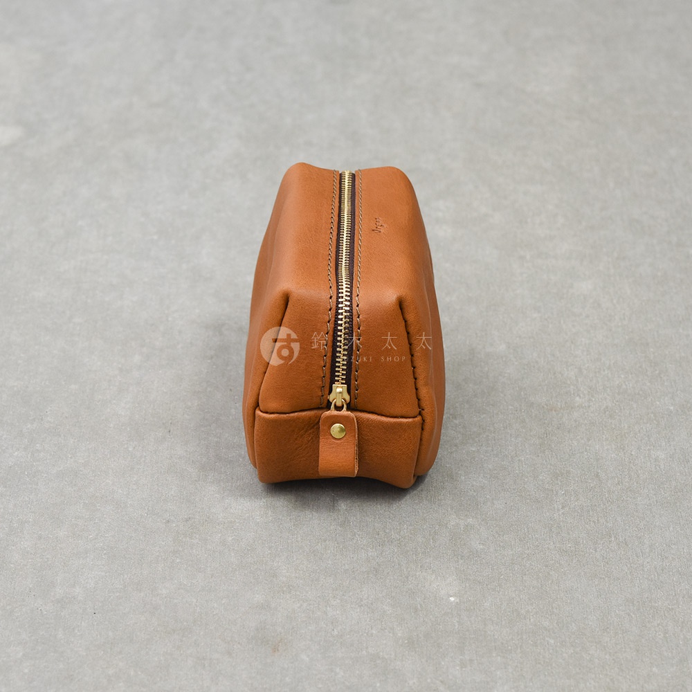 一個直立擺放的HERZ Organ系列棕色皮革拉鍊收納包，皮革質感細膩溫潤，頂部設有黃銅拉鍊與精緻的皮革拉環，邊緣縫線工整，整體呈現簡約且堅固的職人手工風格，背景為淺灰色水泥材質。