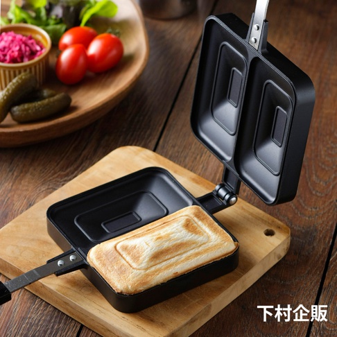 直火式壓邊吐司烤盤，黑色，帶有兩個方形烤盤，一側烤盤內有一個金黃色的吐司，烤盤上帶有銀色金屬手柄，整體放置在木質砧板上。