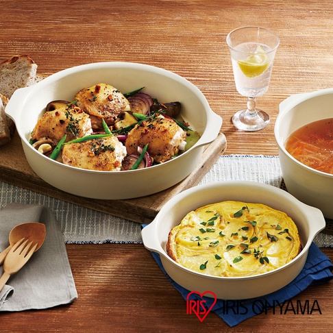 淺米色陶瓷不沾平底鍋，內盛烤雞腿、蔬菜和馬鈴薯烘蛋，搭配一杯檸檬水，展現多樣烹飪成果。