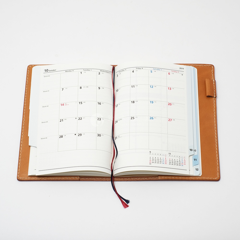 職人手作皮革B6記事本書套，淺棕色皮革，內頁為月曆，附有藍色及紅色書籤帶，皮革邊緣有縫線。