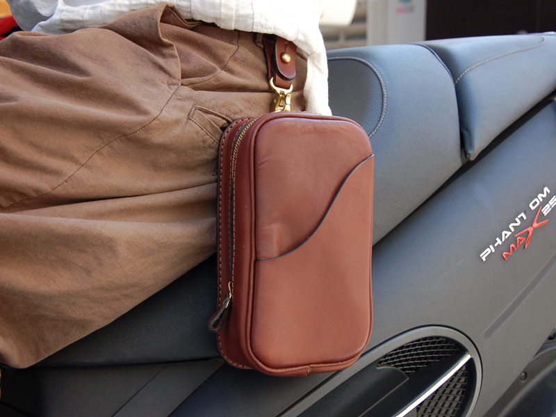 職人手作皮革兩用直立型斜背包，採用深棕色皮革，附有拉鍊開合與金屬掛環，可直接掛於腰帶上。