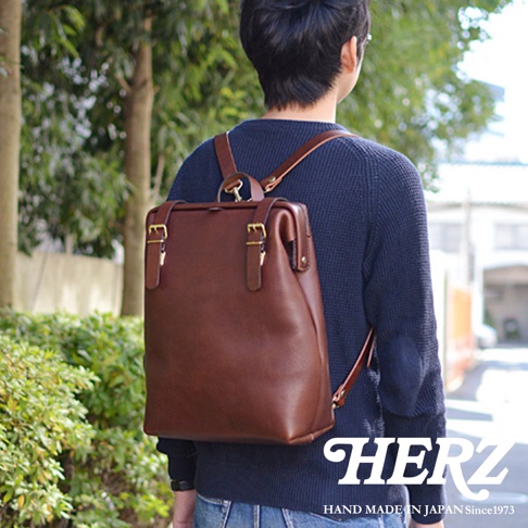 一位男性身背著一個棕色的皮革後背包，背包上有兩個金屬扣和皮質肩帶。