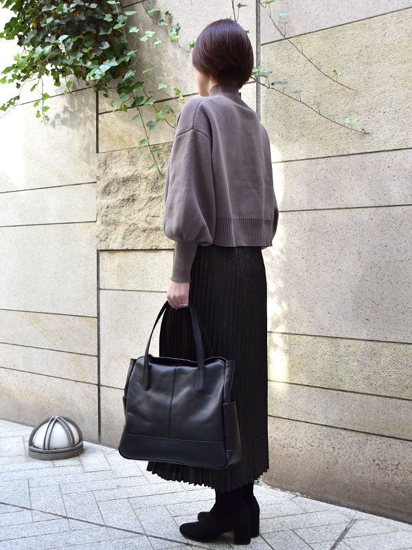 黑色皮革直式托特包，帶有兩個側袋和頂部提把，以簡約縫線裝飾。