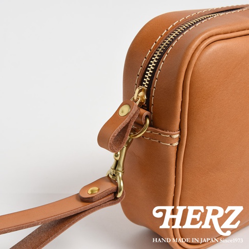 咖啡色皮革手提包，配有可拆卸的金色扣環和皮革腕帶。包包採用縫線工藝，拉鍊為金色。