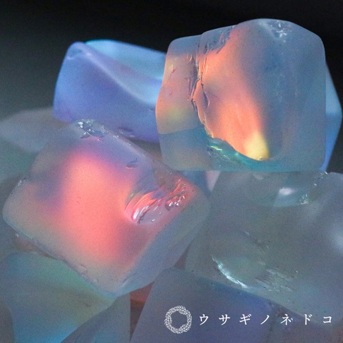 多個透明稜鏡狀的合光石，表面光滑，內部呈現粉紅、橙色和藍色的光影效果，材質看似玻璃或水晶。