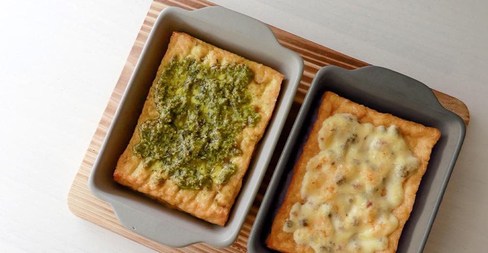 兩個陶製烤盤，一個裝有青醬烤物，另一個裝有起司烤物，烤盤為灰色與淺灰色，長方形，附有提把。