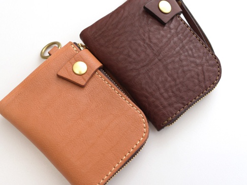 兩款職人手作皮革短夾，一款為棕褐色，另一款為深棕色，皆採用獅鬃風皮革製作，配有黃銅色金屬拉鍊、按扣及掛環。