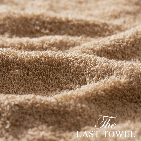 The LAST TOWEL 魔法瞬吸純棉柔毛巾，特寫展示其柔軟蓬鬆的純棉毛圈材質，呈現溫暖的淺褐色調，毛巾表面有自然的褶皺紋理。