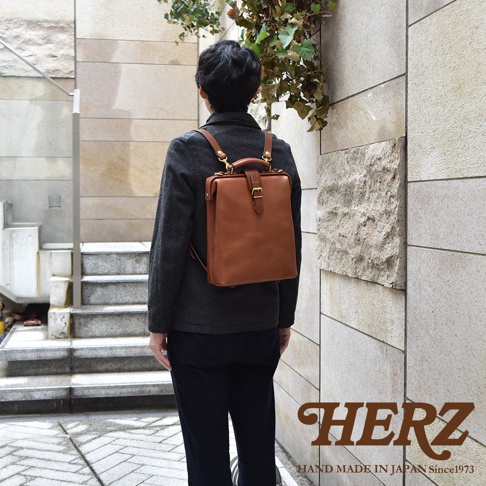 職人手作皮革軟式杜勒斯包，焦糖色皮革，方形包身，配有金屬扣環和提把，可轉換為後背包，展現經典復古風格。