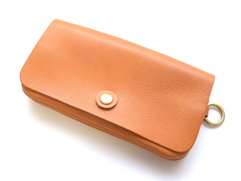 橘色皮革長夾，帶有金色按扣和側邊金屬環，適合旅行使用，多層次收納設計。