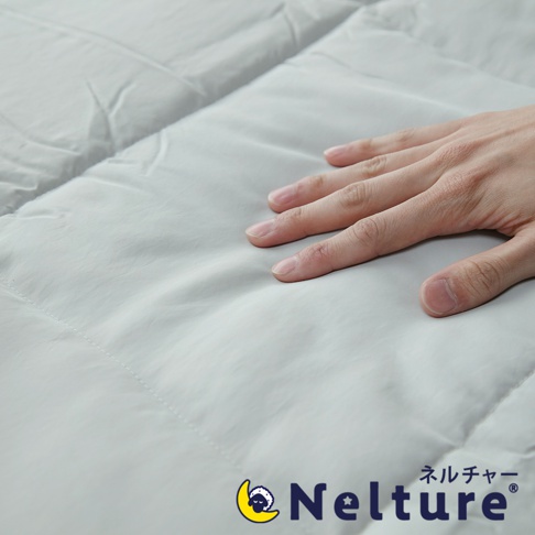 一隻手放在淺灰色、絎縫的 Nemulia 五層散熱涼感單人被上，被子材質光滑，有細緻的紋理。