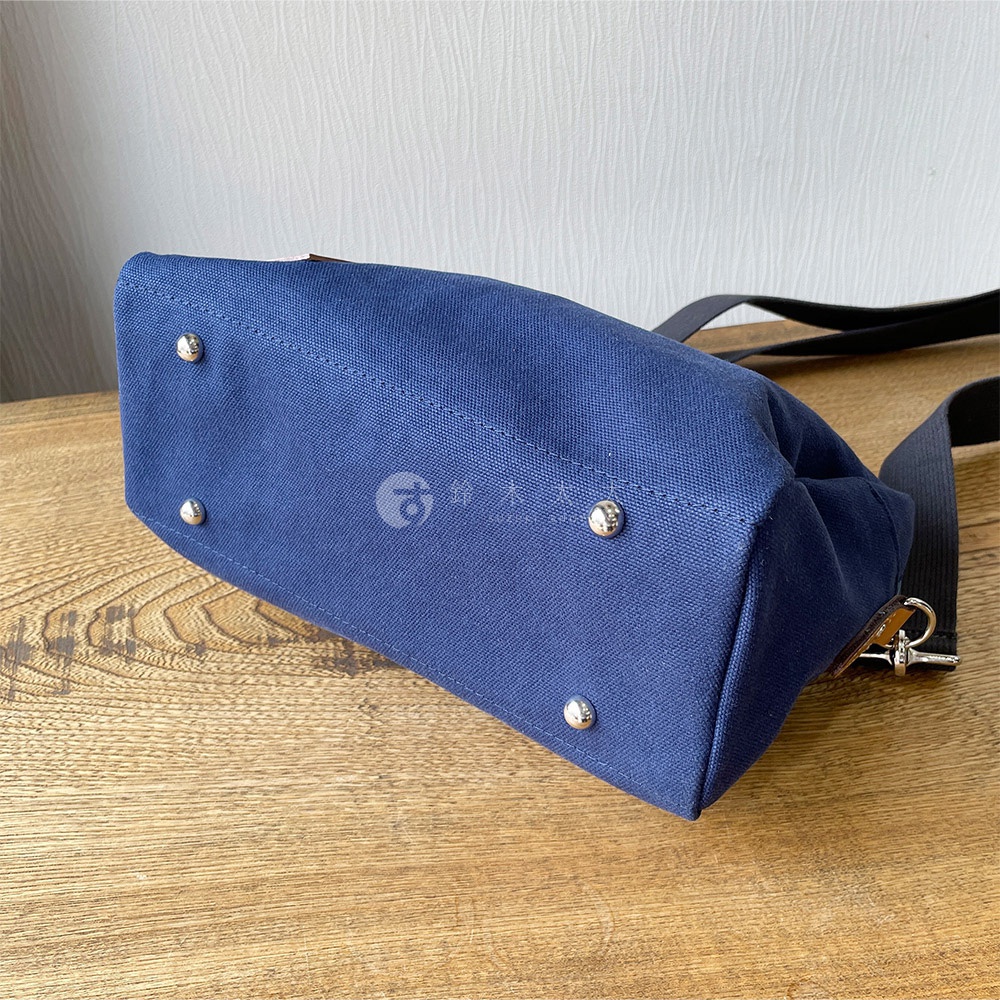 深藍色石洗帆布旅行側背包底部，有四個金屬腳釘，一條黑色揹帶。