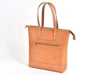 職人手作皮革威靈頓直式拉鍊托特包，天然皮革材質，淺棕色，配有頂部拉鍊開合、正面拉鍊口袋、兩個金屬鉚釘裝飾的皮片，以及一對長手提帶。