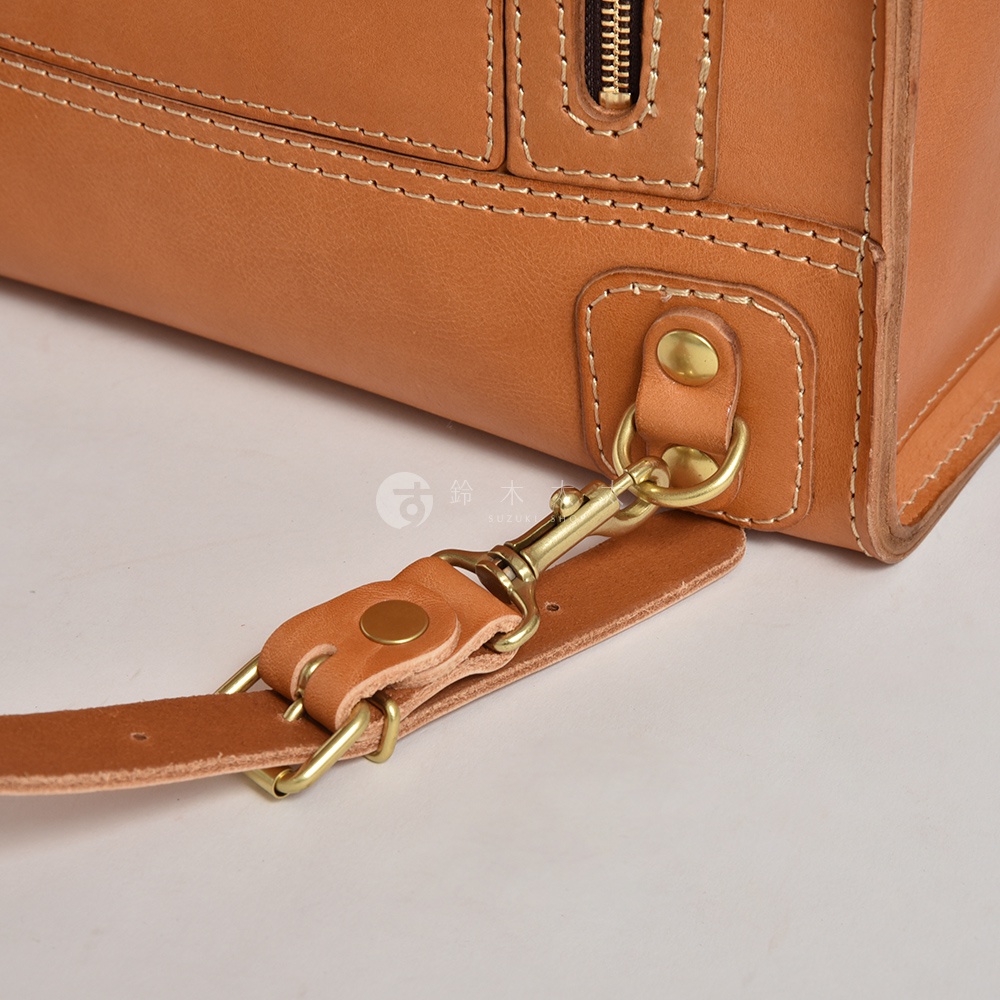 職人手作皮革後背包，採用棕色皮革，搭配黃銅色金屬扣環與拉鍊。包身縫線清晰，細節處有皮革加固與金屬鉚釘。