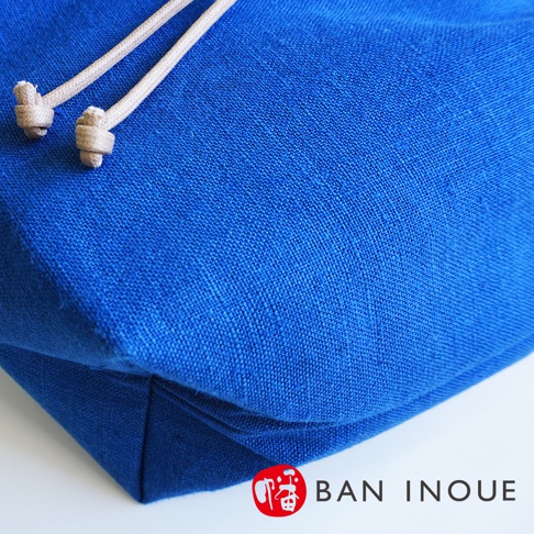 BAN INOUE 藍色束口手提包的特寫，織品紋理清晰可見，繩索繫結處細節明顯。