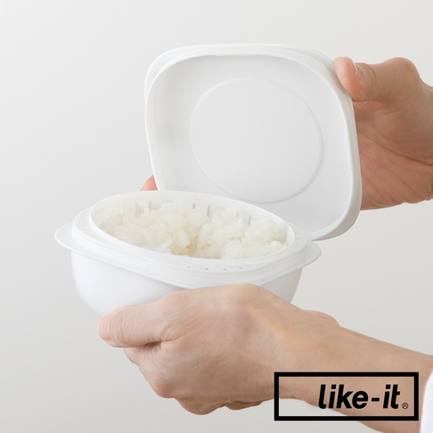 白色雙層蒸氣循環保鮮盒，內含已煮熟的米飯，盒蓋被一隻手打開，另一隻手扶著保鮮盒。