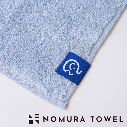 野村毛巾品牌標誌，印有大象圖案的藍色布標，以及印有 NOMURA TOWEL 字樣的品牌標籤。